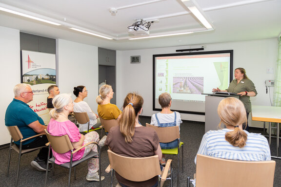 Eine Frau hält eine Fortbildung in einem Besprechungsraum. Eine kleine Gruppe hört ihr dabei zu.