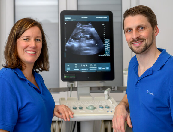 Dr. med. Caroline Eich und Dr. med. Michael Korten stehene vor einem Ultraschallbild, welches am Computer angezeigt wird und lächeln in die Kamera. 